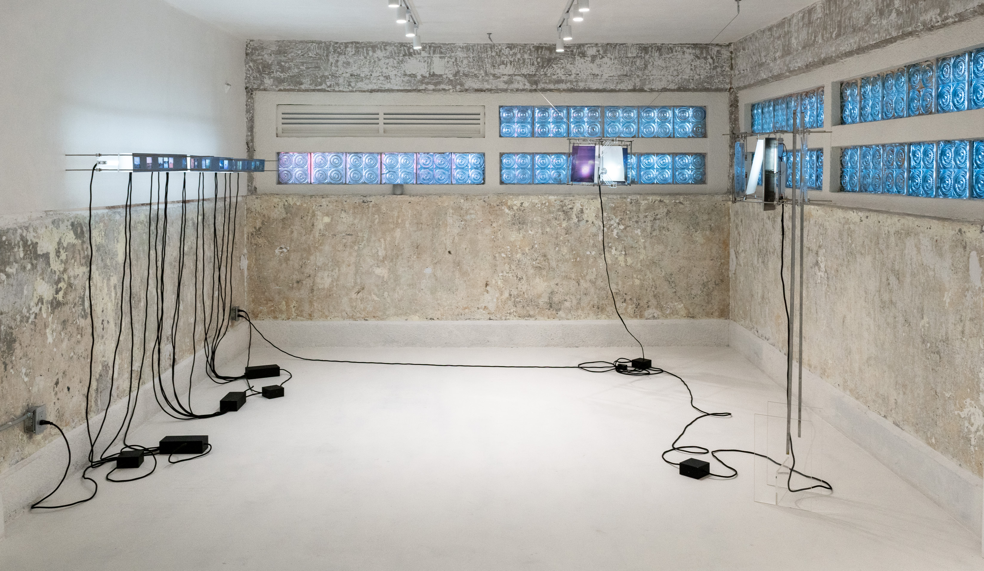 Vista de instalación en sala con muros texturizados y ventanas de bloque de vidrio azul