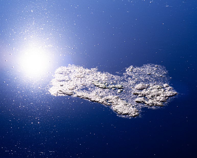 Sol reflejado sobre agua azul profunda con una mancha de espuma blanca